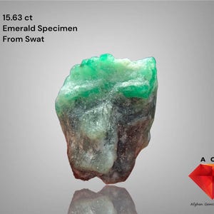 May include: A rough-cut emerald specimen from Swat, Pakistan, weighing 15.63 carats. The gemstone has a vibrant green hue with a crystalline structure. The image includes text that reads "Emerald Specimen From Swat".