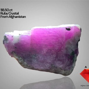 May include: A raw ruby crystal from Afghanistan, weighing 118.50 carats. The gemstone displays a vibrant pink hue with areas of white and gray. The image includes text that reads "118.50 ct Ruby Crystal From Afghanistan."