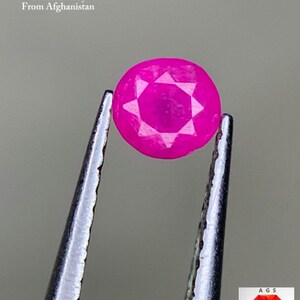 Pode incluir: Uma gema de rubi facetada rosa brilhante, segurada por pinças. A gema tem um padrão em forma de estrela em sua superfície. O texto na imagem diz "0,23 ct Rubi Facetado Do Afeganistão."