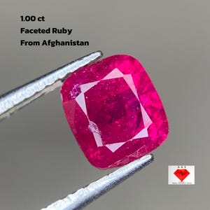 Puede incluir: Un rubí facetado con corte cojín, sostenido por unas pinzas. El rubí es de color rojo vibrante y parece transparente. El texto en la imagen dice "1.00 ct Faceted Ruby From Afghanistan."