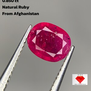 Puede incluir: Un rubí natural ovalado de Afganistán, de color rojo intenso, sujeto con pinzas. La gema pesa 0,850 ct. La imagen incluye el texto "Natural Ruby From Afghanistan".