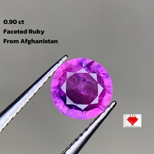 Peut inclure: Un rubis facetté d'Afghanistan, tenu par une pince. La gemme est d'un rose profond avec un motif en forme d'étoile au centre. Le texte sur l'image indique "0,90 ct Faceted Ruby From Afghanistan."