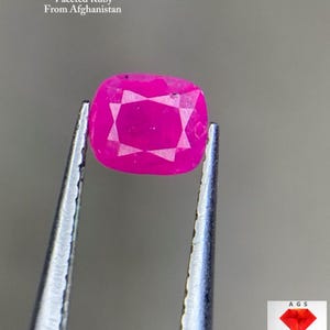 Może przedstawiać: Fasetowany rubin o szlifie poduszkowym, trzymany pęsetą. Żywy różowy kamień szlachetny waży 0,57 ct i pochodzi z Afganistanu. Obraz zawiera tekst: "0.57 ct Faceted Ruby From Afghanistan."