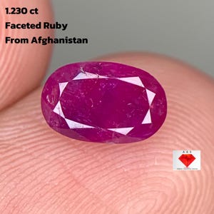 Pode incluir: Uma gema de rubi facetada de 1,230 ct do Afeganistão. A gema ovalada é de um vermelho profundo e vibrante com múltiplas facetas. O texto na imagem diz "Faceted Ruby From Afghanistan".