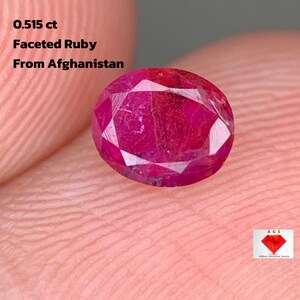 Könnte beinhalten: Ein facettierter Rubin aus Afghanistan, mit einem Gewicht von 0,515 ct. Der oval geformte Edelstein ist ein tiefes, leuchtendes Rot mit mehreren Facetten. Der Text "0.515 ct Faceted Ruby From Afghanistan" ist ebenfalls enthalten.