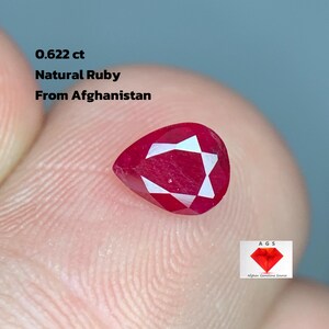 Könnte beinhalten: Ein tropfenförmiger, facettierter Natur-Rubin aus Afghanistan, mit einem Gewicht von 0,622 ct. Der Rubin hat eine tiefrote Farbe mit weißen Innenreflexionen. Der Text "Natural Ruby From Afghanistan" ist ebenfalls enthalten.