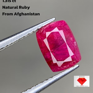 May include: A natural ruby from Afghanistan, weighing 1.315 ct, is held by tweezers. The gemstone is a deep pinkish-red with a geometric, white internal pattern. The image includes text: "1.315 ct Natural Ruby From Afghanistan."