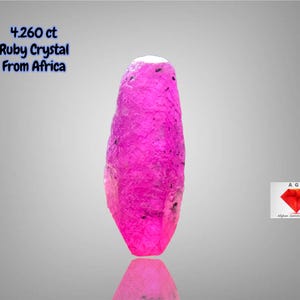以下が含まれることがあります： アフリカ産の鮮やかな細長いルビーの結晶、4.260 ct。宝石は濃いピンク色で、表面はざらざらしています。画像には「4.260 ct Ruby Crystal From Africa」というテキストが含まれています。
