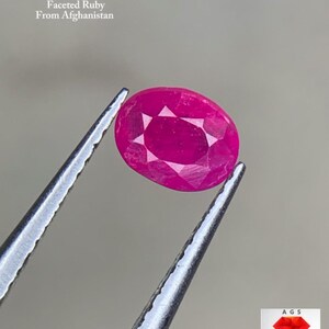 May include: A faceted, oval ruby held by tweezers. The gemstone is a vibrant pink-red colour and has a star-like pattern in the centre. Text in the image reads "0.54 ct Faceted Ruby From Afghanistan."