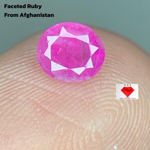 Op de afbeelding: Een gefacetteerde robijn van 0,55 ct, afkomstig uit Afghanistan. De edelsteen heeft een levendige roze kleur met een stervormig patroon van witte facetten. De tekst "0.55 ct Faceted Ruby From Afghanistan" is ook zichtbaar.