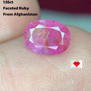 Puede incluir: Una gema de rubí facetada de 1,55 ct de Afganistán. La gema de forma ovalada es de un rojo rosado vibrante con facetas blancas. El texto "1.55ct Faceted Ruby From Afghanistan" es visible.