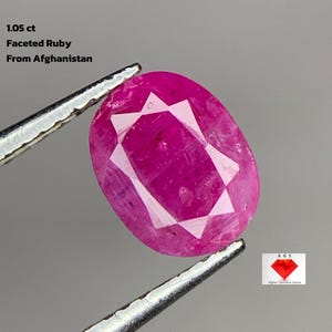 Könnte beinhalten: Ein facettierter Rubin, 1,05 ct, gehalten von einer Pinzette. Der oval geformte Edelstein hat eine leuchtende rosa-rote Farbe mit inneren Facetten. Der Text auf dem Bild lautet "Faceted Ruby From Afghanistan".
