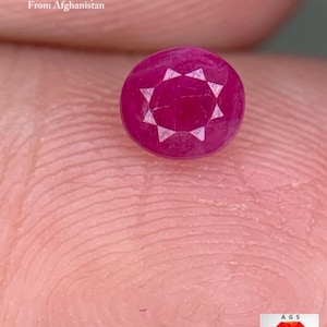 Könnte beinhalten: Ein facettierter, runder Rubin-Edelstein, 0,47 ct, aus Afghanistan. Der Rubin hat eine tiefe, satte rote Farbe mit einem sternförmigen Facettenmuster auf der Oberfläche. Der Text "0.47 ct Faceted Ruby From Afghanistan" ist sichtbar.