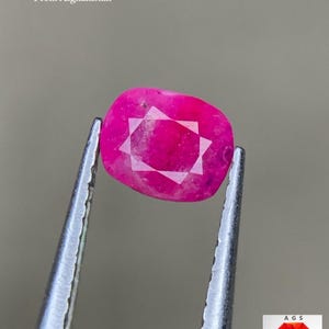 Peut inclure: Une pierre précieuse rubis facettée d'Afghanistan, tenue par une pince. La gemme est d'un rose vif avec un motif en forme d'étoile au centre. Le texte indique "0,59 ct Rubis Facetté D'Afghanistan."