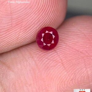 Puede incluir: Una gema de rubí facetada, de aproximadamente 0,53 quilates, de Afganistán. La piedra redonda, de color rojo intenso, tiene un patrón de estrella en el centro. El texto "0.53 ct Faceted Ruby From Afghanistan" es visible.