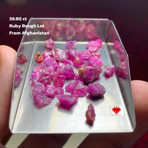 Puede incluir: Un lote de gemas de rubí en bruto, exhibidas en una pequeña bandeja plateada. Las gemas son de un color rojo rosado vibrante. El texto en la imagen dice: "39.80 ct Ruby Rough Lot From Afghanistan."