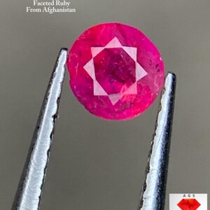 Op de afbeelding: Een gefacetteerde robijn uit Afghanistan, vastgehouden door een pincet. De robijn heeft een levendige roze-rode kleur, met een wit stervormig ontwerp in het midden. De tekst op de afbeelding luidt "0,26 ct Faceted Ruby From Afghanistan."