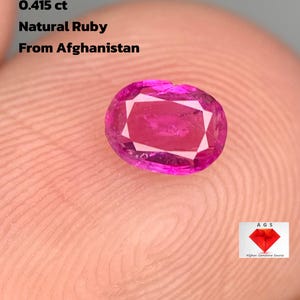 Könnte beinhalten: Ein lebendiger, oval geschliffener Naturrubin aus Afghanistan, mit einem Gewicht von 0,415 ct. Der Edelstein zeigt eine satte rosa Farbe mit inneren Facetten. Der Text "Natural Ruby From Afghanistan" ist ebenfalls enthalten.