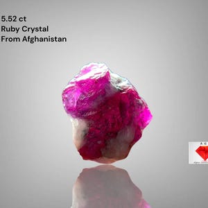 Puede incluir: Cristal de rubí en bruto de 5,52 ct de Afganistán. La gema muestra un color rojo rosado intenso con una superficie reflectante. La imagen incluye texto que indica el peso y el origen del cristal.