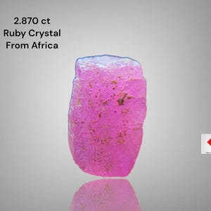 Könnte beinhalten: Ein leuchtend rosa Rubinkristall aus Afrika, mit einem Gewicht von 2,870 ct. Der Edelstein hat eine raue, strukturierte Oberfläche und eine natürliche, unregelmäßige Form. Das Bild enthält den Text "2.870 ct Ruby Crystal From Africa".