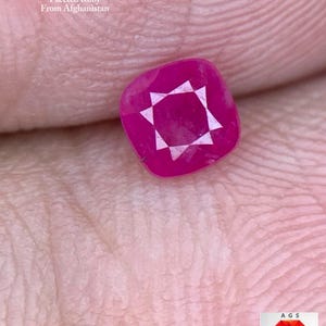 May include: A faceted, cushion-cut ruby gemstone, weighing 0.53 ct, with a starburst pattern in the center. The ruby is a deep pinkish-red colour. Text on the image reads "0.53 ct Faceted Ruby From Afghanistan".