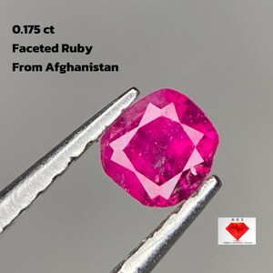 May include: A faceted ruby from Afghanistan, held by tweezers. The gemstone is a vibrant pinkish-red color and has a square shape with multiple facets. Text on the image reads: 0.175 ct, Faceted Ruby, From Afghanistan.