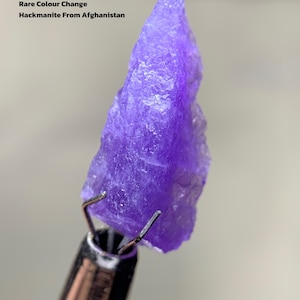 Puede incluir: Una vibrante gema de Hackmanita púrpura de Afganistán, sujeta por una herramienta de metal. La imagen incluye el texto "4.06 ct Rare Colour Change Hackmanite From Afghanistan."