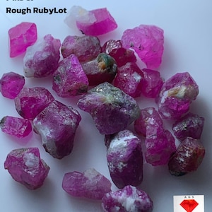 May include: A collection of rough ruby gemstones in varying sizes and shapes, displaying a vibrant pink hue with some white and green inclusions. The image includes the text "74.13 ct Rough RubyLot".