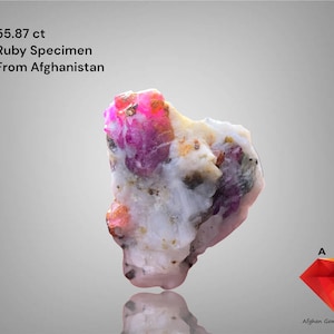 Puede incluir: Un espécimen de rubí de 55,87 ct de Afganistán. La gema presenta una mezcla de colores rosa, rojo, blanco y beige. El texto "Ruby Specimen From Afghanistan" se muestra encima.