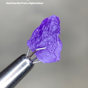 Puede incluir: Una vibrante gema de Hackmanita púrpura de Afganistán, sostenida por una herramienta plateada. La piedra es de 3,51 ct y exhibe un raro cambio de color. El texto en la imagen dice: "Rare Colour Change" y "Hackmanite From Afghanistan."