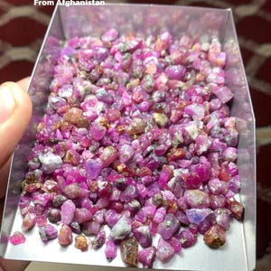 Op de afbeelding: Een bakje gevuld met een ruwe partij robijn edelstenen. De edelstenen zijn een mix van roze, rode en bruine tinten. De tekst op de afbeelding luidt "532 ct Ruby Rough Lot From Afghanistan."
