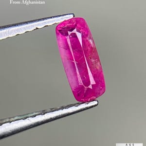 May include: A faceted ruby gemstone from Afghanistan, held by tweezers. The ruby is a vibrant pinkish-red colour and weighs 0.28 ct. The image includes text that reads "0.28 ct Faceted Ruby From Afghanistan."