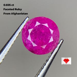Puede incluir: Un rubí facetado de corte redondo, sostenido por unas pinzas. La gema es de un color rojo-rosa vibrante. El texto en la imagen dice: "0.835 ct Faceted Ruby From Afghanistan."