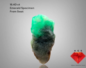 May include: A raw emerald specimen from Swat, Pakistan, weighing 16.40 ct. The gemstone features a vibrant green hue at the top, transitioning to darker shades towards the base. The image includes text that reads "Emerald Specimen From Swat".