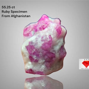 May include: A natural ruby specimen from Afghanistan, weighing 55.25 ct. The gemstone features a mix of pink and white hues. The image includes text indicating the origin and weight of the ruby.