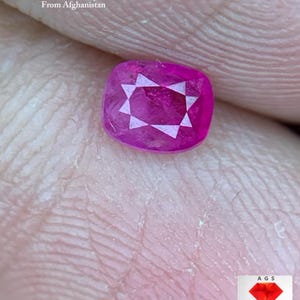 Puede incluir: Una gema de rubí facetada con corte cojín, de 0,36 ct, de Afganistán. La gema es de un color rojo rosado vibrante con un patrón en forma de estrella en el centro. El texto "0.36 ct Faceted Ruby From Afghanistan" es visible.