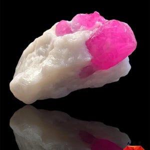 Pode incluir: Um espécime de rubi de 152 ct com uma estrutura cristalina rosa vibrante e profunda incrustada numa matriz mineral branca, opaca e rugosa. A pedra preciosa bruta apresenta uma forma natural irregular com uma textura brilhante.