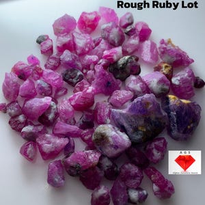May include: A collection of rough ruby gemstones, with a total weight of 168.69 carats. The rubies are various shades of pink and red, with some having a translucent appearance. The image includes the text "Rough Ruby Lot".