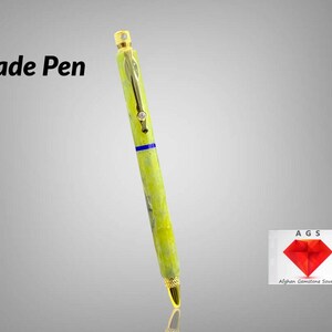 May include: A jade green pen with gold accents and a blue stripe. The pen has a diamond-shaped design on the top and bottom. The pen is made by Afghan Gemstone Source.