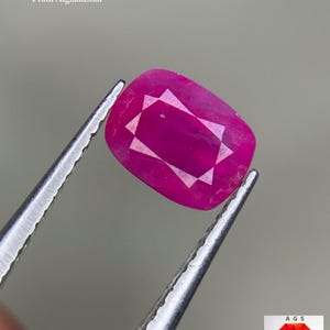 Puede incluir: Un rubí facetado, sostenido por unas pinzas. La gema es de color rosa-rojo vibrante, con forma rectangular y facetas internas. El texto en la imagen dice "1.17 ct Faceted Ruby From Afghanistan."