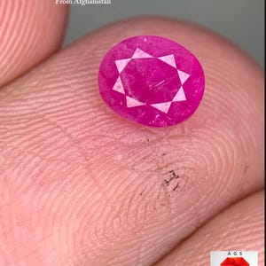 Pode incluir: Uma gema de rubi facetada em forma oval, 0,90 ct, do Afeganistão. O rubi é de uma cor rosa-vermelha vibrante com um padrão em forma de estrela no centro. A imagem também inclui o texto "0,90 ct Rubi Facetado Do Afeganistão".