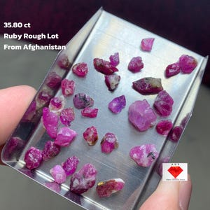 May include: A collection of rough ruby gemstones in varying shades of pink and red, displayed on a silver tray. The text on the image reads "35.80 ct Ruby Rough Lot From Afghanistan."