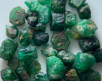 Op de afbeelding: Een verzameling ruwe smaragden, met een gewicht van 72,05 ct. De edelstenen variëren in vorm en grootte en vertonen verschillende groentinten. De tekst "Rough Emerald Lot" is zichtbaar.