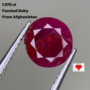 Könnte beinhalten: Ein facettierter Rubin aus Afghanistan, gehalten von einer Pinzette. Der Rubin hat eine tiefrote Farbe mit einem sternförmigen Facettenmuster. Text auf dem Bild: "1.970 ct Faceted Ruby From Afghanistan."
