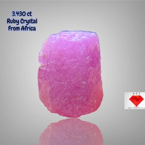 Könnte beinhalten: Ein leuchtend rosa Rubinkristall aus Afrika, mit einem Gewicht von 3,430 ct. Der rohe Edelstein hat eine strukturierte Oberfläche und spiegelt sich darunter. Der Text auf dem Bild lautet "3.430 ct Ruby Crystal From Africa".