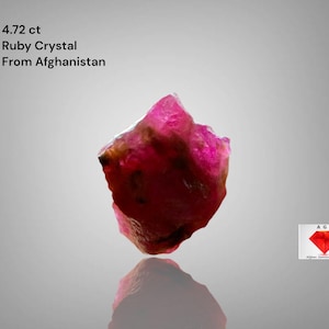 Puede incluir: Cristal de rubí en bruto de 4,72 ct de Afganistán. La gema es de color rojo intenso con una superficie rugosa y texturizada. La imagen incluye el texto "4.72 ct Ruby Crystal From Afghanistan."