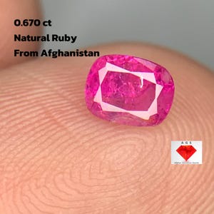 Puede incluir: Un rubí natural rosa vivo, talla cojín, de Afganistán, con un peso de 0,670 ct. La gema presenta un patrón geométrico que refleja la luz. La imagen incluye el texto "0.670 ct Natural Ruby From Afghanistan."