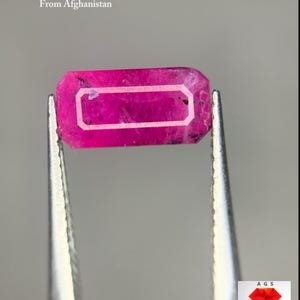Puede incluir: Un rubí facetado de Afganistán, sujeto con pinzas. El rubí es de color rosa vibrante, de forma rectangular y con un borde blanco. El texto en la imagen dice "1.26 ct Faceted Ruby From Afghanistan."