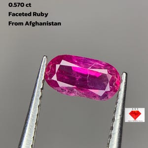 May include: A faceted ruby from Afghanistan, held by tweezers. The gemstone is a vibrant pinkish-red colour, with visible facets. Text on the image reads: "0.570 ct Faceted Ruby From Afghanistan."