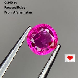 Puede incluir: Un rubí facetado y redondo, sostenido por unas pinzas. El rubí es de color rosa vibrante y está etiquetado como 0,240 ct y de Afganistán. La imagen también incluye el texto "Afghan Gemstone Source".